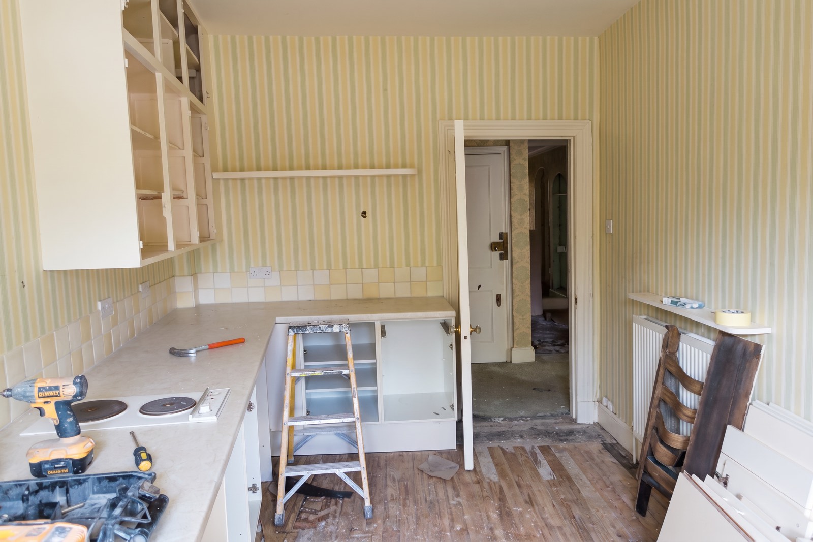 Old kitchen part-stripped, with doorless wall units, tools on the worktop and a stepladder