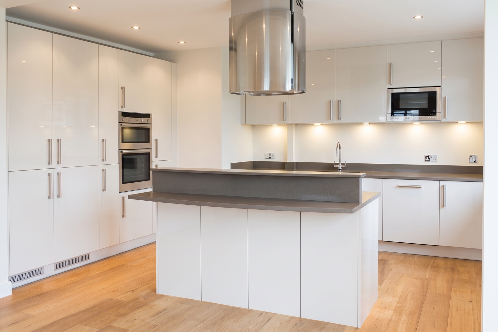 Finished kitchen with white gloss units, grey-topped island and oak floor
